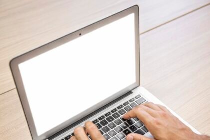 digital: Un gros plan des mains d'une personne tapant sur un ordinateur portable avec un smartphone à proximité sur un bureau en bois, symbolisant la révolution numérique de 2026 en Côte d'Ivoire qui comble le fossé de communication entre le gouvernement et ses citoyens.