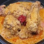 Gastronomie: Un bol appétissant de sauce pistache traditionnelle ivoirienne (soupe de graines de courge) servie avec des morceaux de viande et de poisson, représentant les riches traditions culinaires et les saveurs festives de la Côte d'Ivoire en 2026.