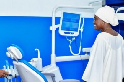 Santé Publique: Un professionnel de santé présentant un équipement dentaire moderne à une visiteuse au nouveau centre médico-scolaire ultra-moderne Mariatou Koné à Boundiali, en mars 2026, illustrant l'investissement de la Côte d'Ivoire dans la santé publique scolaire.